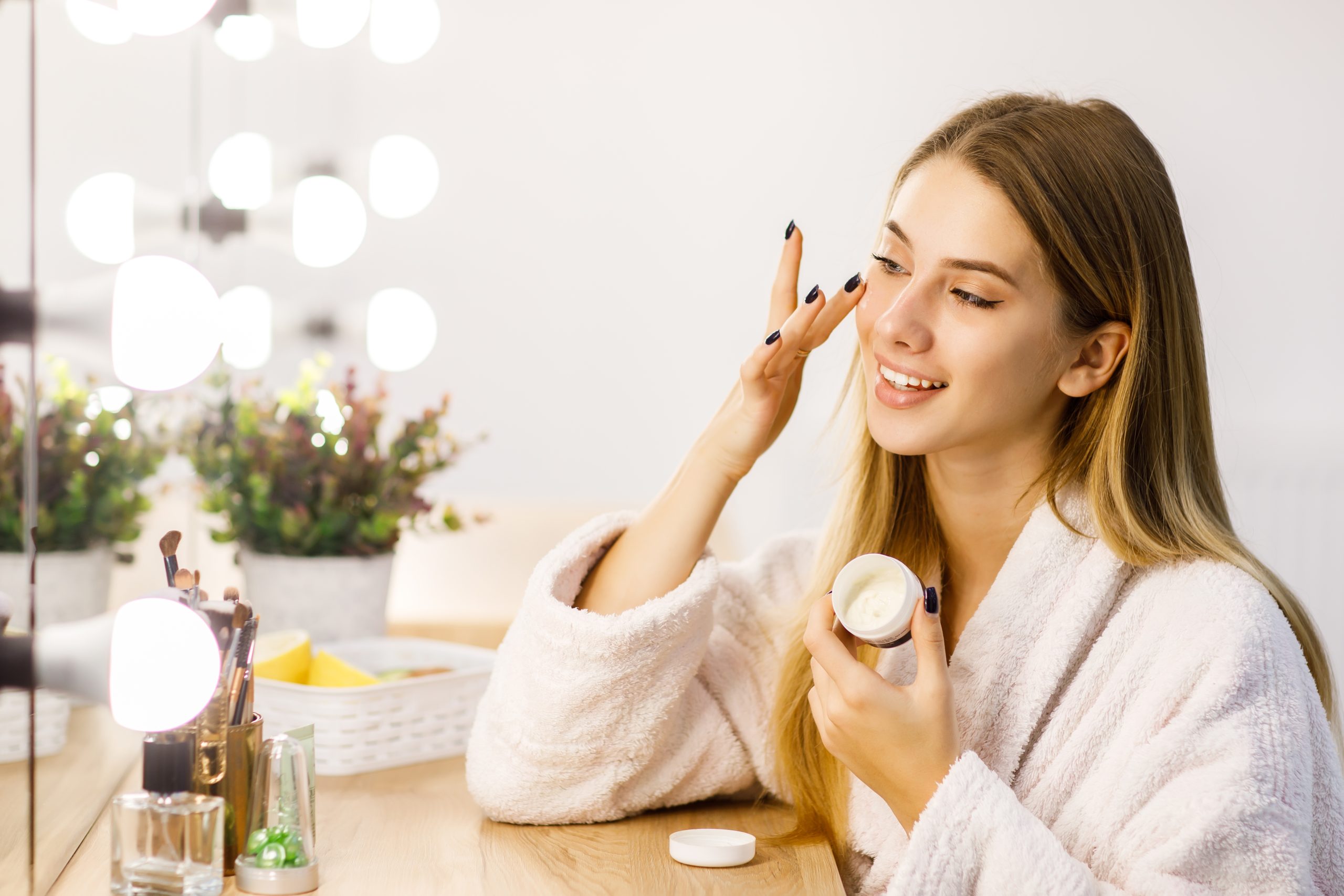 young beautiful blonde girl cares face skin with moisturizer front mirror scaled